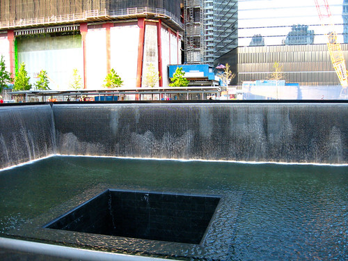 A large square recessed pool, with a smaller square hole in the middle. There are building under construction on the other side of the pool.