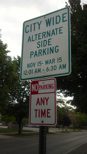 A sign reads: "City wide alternate side parking Nov 15-Mar 15, 12:01 am-6:30 am". Below is another sign prohibiting parking (at this location) at any time.