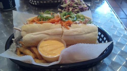 A bánh mì sandwich served with fries and some yellow sauce on top of thin white waxed paper on a green tray.