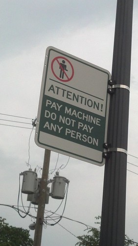 A sign attached to a pole with a no-slash through a person and the text "Attention! Pay machine. Do not pay any person."